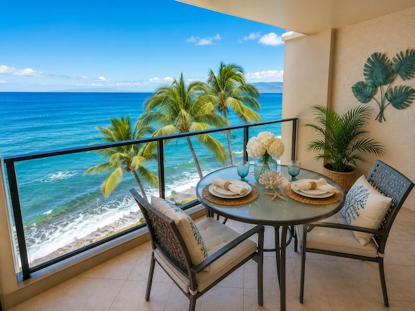 A balcony with a table set for two, overlooking a beach with palm trees and the ocean.