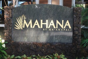 A sign with the text "MAHANA AT KA'ANAPALI" surrounded by a stone wall and greenery. - Oceanfront Mahana Condo  1BR/1BA Sweeping Views Ac, Pool (Lahaina)