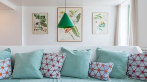 Une pièce avec un canapé bleu clair, des coussins à motifs et des reproductions encadrées de plantes ornant le mur.