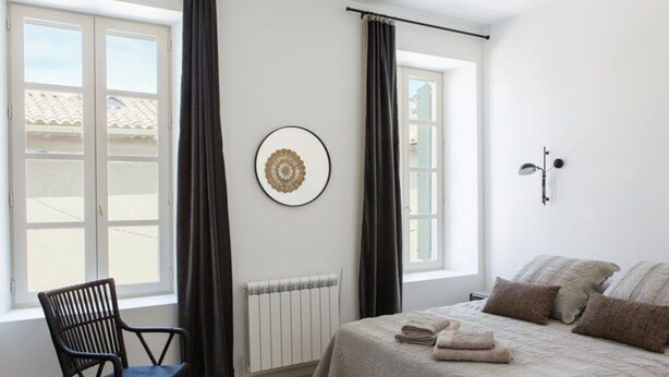 Une chambre à coucher avec un lit, une chaise, un radiateur et une fenêtre avec des rideaux.