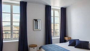 Une chambre à coucher avec un lit, une table de chevet, un miroir et une fenêtre avec des rideaux.