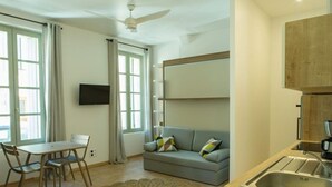 Un salon moderne comprenant un canapé, une table à manger avec des chaises, un téléviseur et un coin cuisine avec un évier.