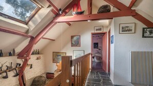 Un interno rustico con soffitto spiovente, travi in legno, pavimento in pietra e vista attraverso uno skylight.
