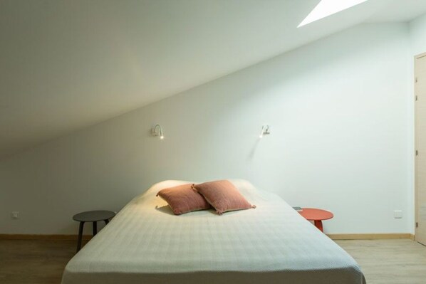 A bedroom with a bed, two wall-mounted lights, a small round table, and a door.