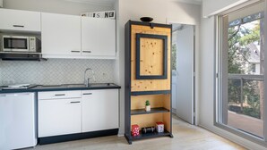 A modern kitchen with white cabinets, a microwave, and a wooden shelf unit with decorative items. - Apartment for 2 adults/2 kids, balcony (La Baule-Escoublac)