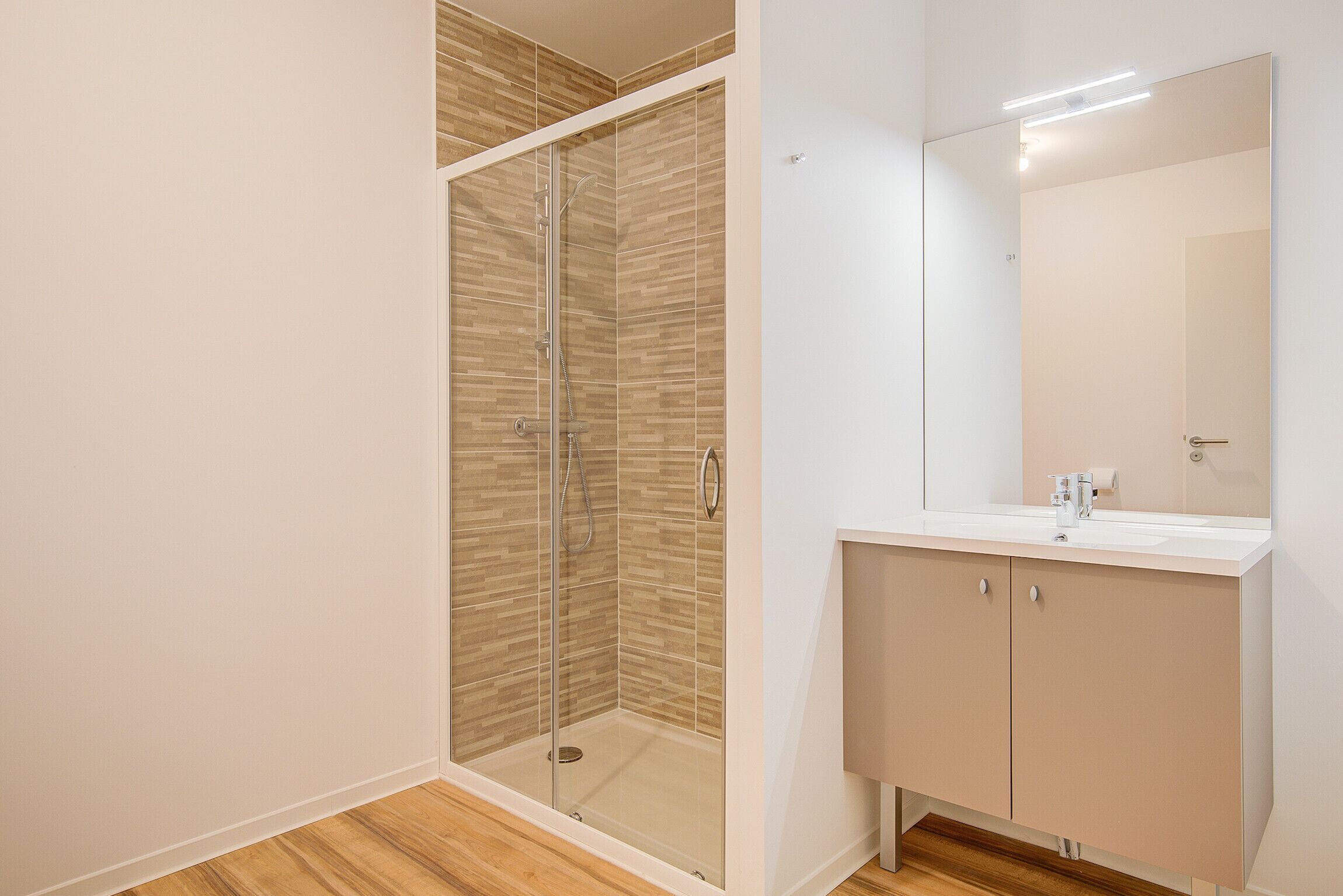 Ein modernes Badezimmer mit einer gläsernen Dusche, einem weißen Waschbecken und einem großen Spiegel.