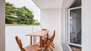 A balcony with a wooden table and chairs, a glass door, and a view of trees. - Relax in this beautiful flat in Lacanau (Lacanau)