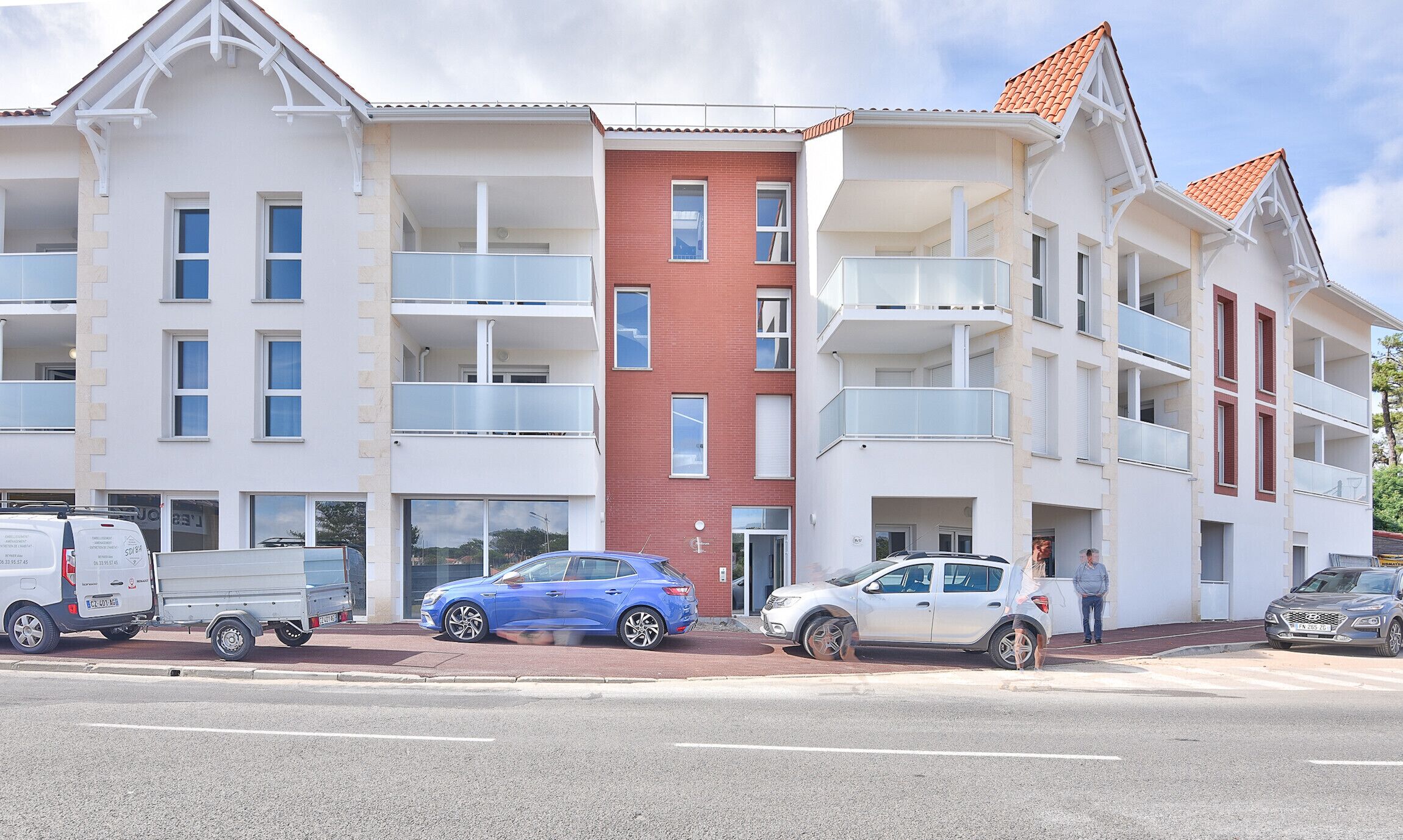 Ein mehrstöckiges Wohngebäude mit Balkonen, einem roten Backsteinbereich und einem Parkplatz mit Autos.