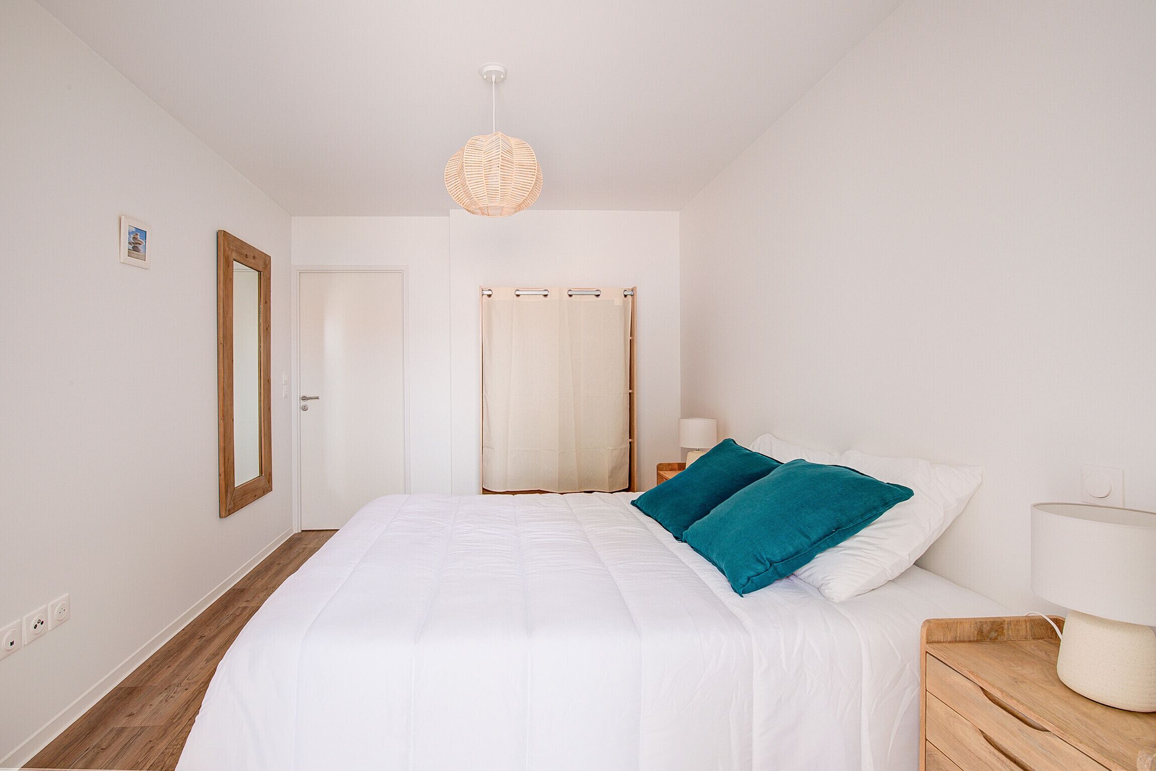 A bedroom with a large bed, a wooden nightstand, a bedside lamp, a mirror, and a door.
