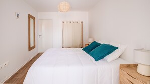 A bedroom with a large bed, a wooden nightstand, a bedside lamp, a mirror, and a door. - Relax in this beautiful flat in Lacanau (Lacanau)