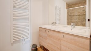 A modern bathroom with a white vanity, two sinks, a large mirror, and a towel rack.
