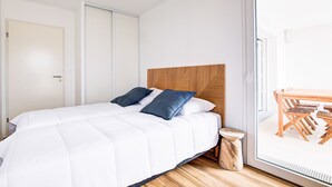 A bedroom with a bed, a wooden headboard, a small stool, and a sliding glass door leading to a dining area.