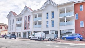 A multi-story building with balconies, a parking area, and a blue car parked on the street.