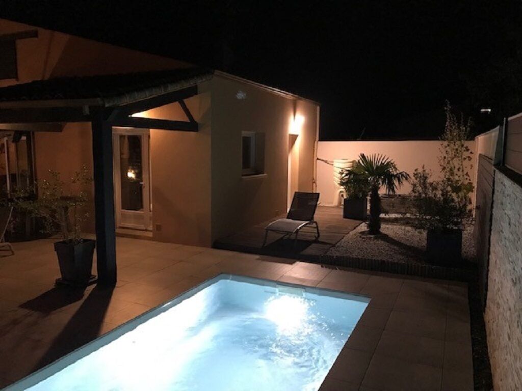 A pool area with a hot tub, a covered seating area, and a small building with a door and windows.
