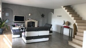 A modern living room with a sofa, a flat-screen TV, and a staircase.
