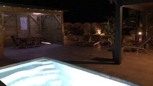 Un espace piscine extérieur doté d’une terrasse en bois, de chaises longues et d’un coin salon abrité.