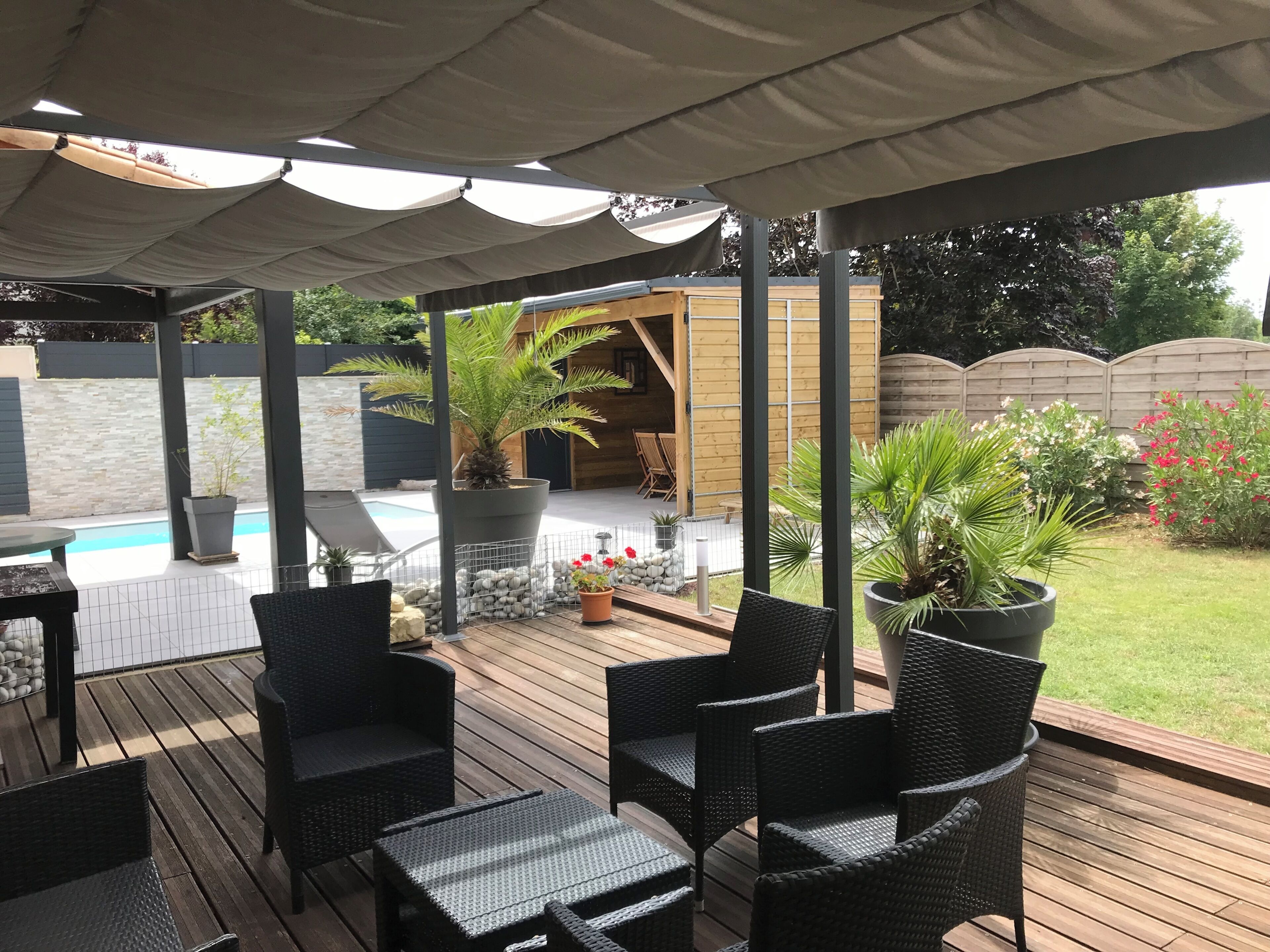 A covered outdoor area with a pool, wicker furniture, and potted plants.
