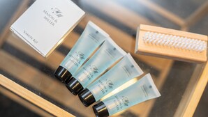 Une trousse de toilette comprenant un miroir, une brosse en bois et trois tubes de gel douche.