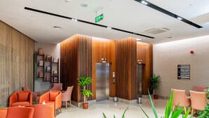 Un vestíbulo moderno con sillones naranja, paneles de madera y un letrero que indica un restaurante y un gimnasio.