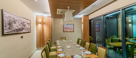 Un salón de conferencias con una mesa larga, sillas tapizadas en verde y techo de madera.