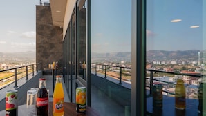 Un balcón con vista a la ciudad, botellas de Coca-Cola, Fanta y Cappy, y una lata de Pripps.