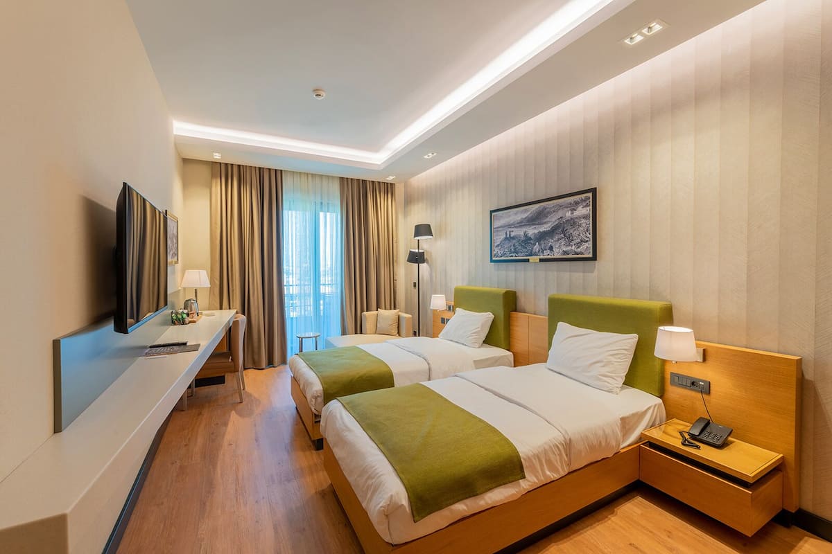 A hotel room with two beds, a desk, a TV, and a painting on the wall.