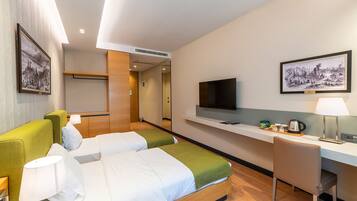 Habitación de hotel con dos camas, un escritorio, un televisor y obras de arte en las paredes.
