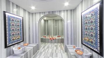 Un baño lujoso con pisos de mármol, un espejo arqueado central y azulejos decorativos.