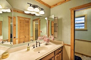A bathroom with a large mirror, wooden cabinets, a sink, and a window with a view.