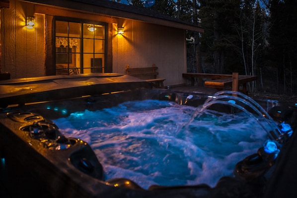 A hot tub with a wooden deck and a bench, surrounded by a wooden fence and trees.