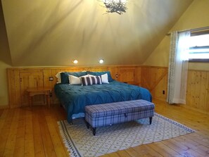 A bedroom with a sloped ceiling, wooden paneling, a bed with blue bedding, a bench, and a patterned rug.