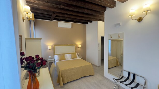 A bedroom with a bed, bedside tables, a mirror, a dresser, and a vase of flowers. - Residenza Briati (Venice)