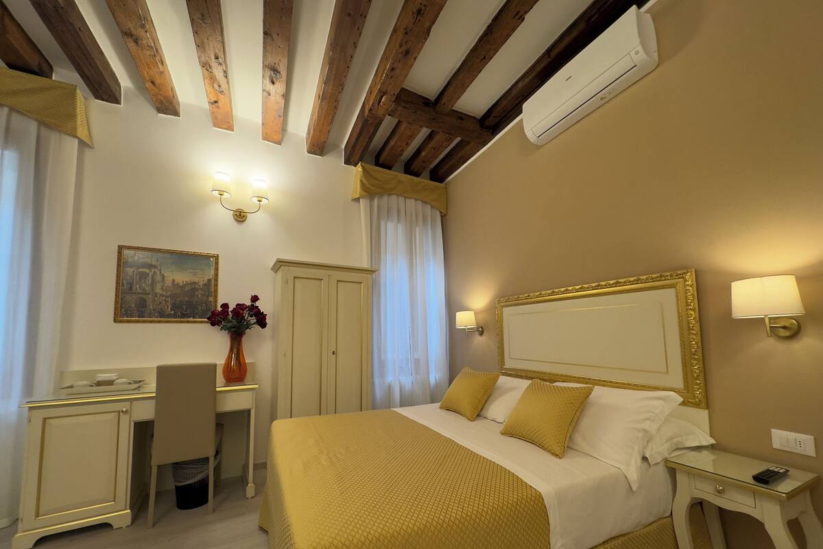 A hotel room with a bed, desk, chair, and a painting on the wall.