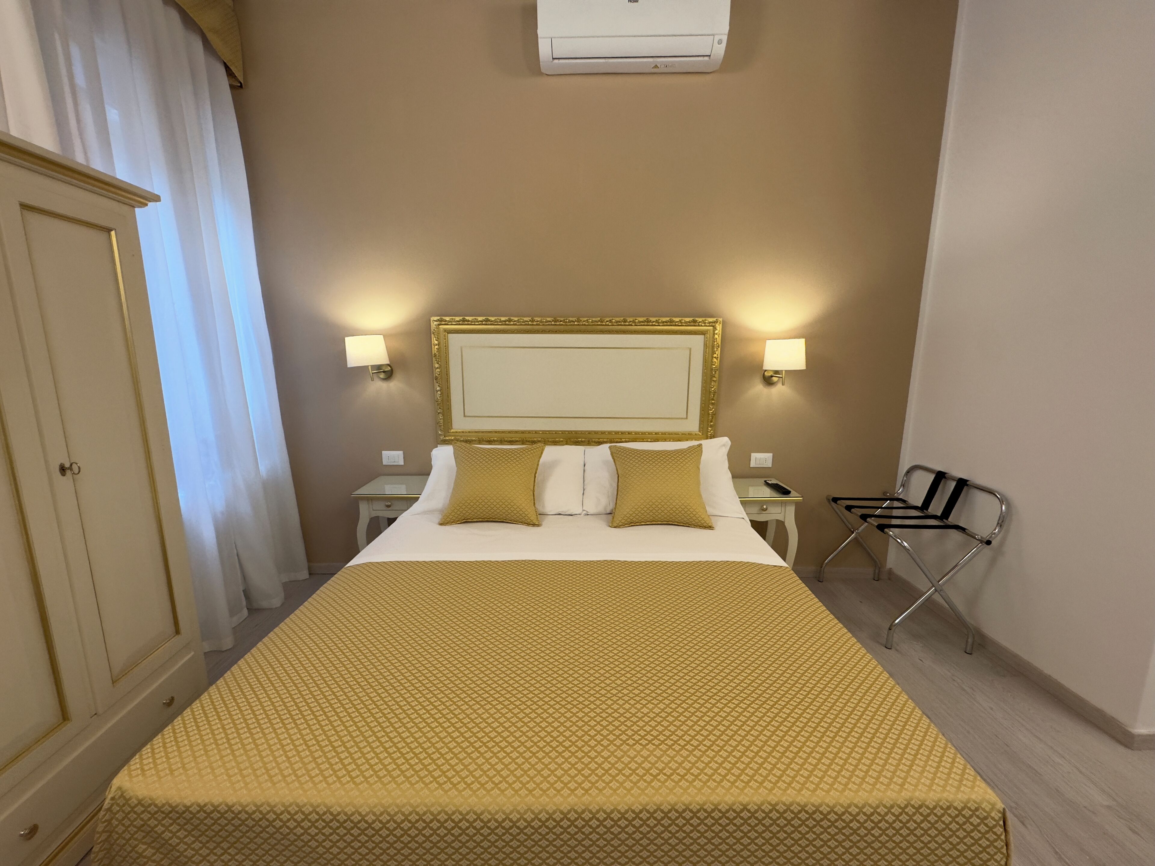 Una habitació d'hotel amb un llit, dues taules de nit, un armari i una cadira.
