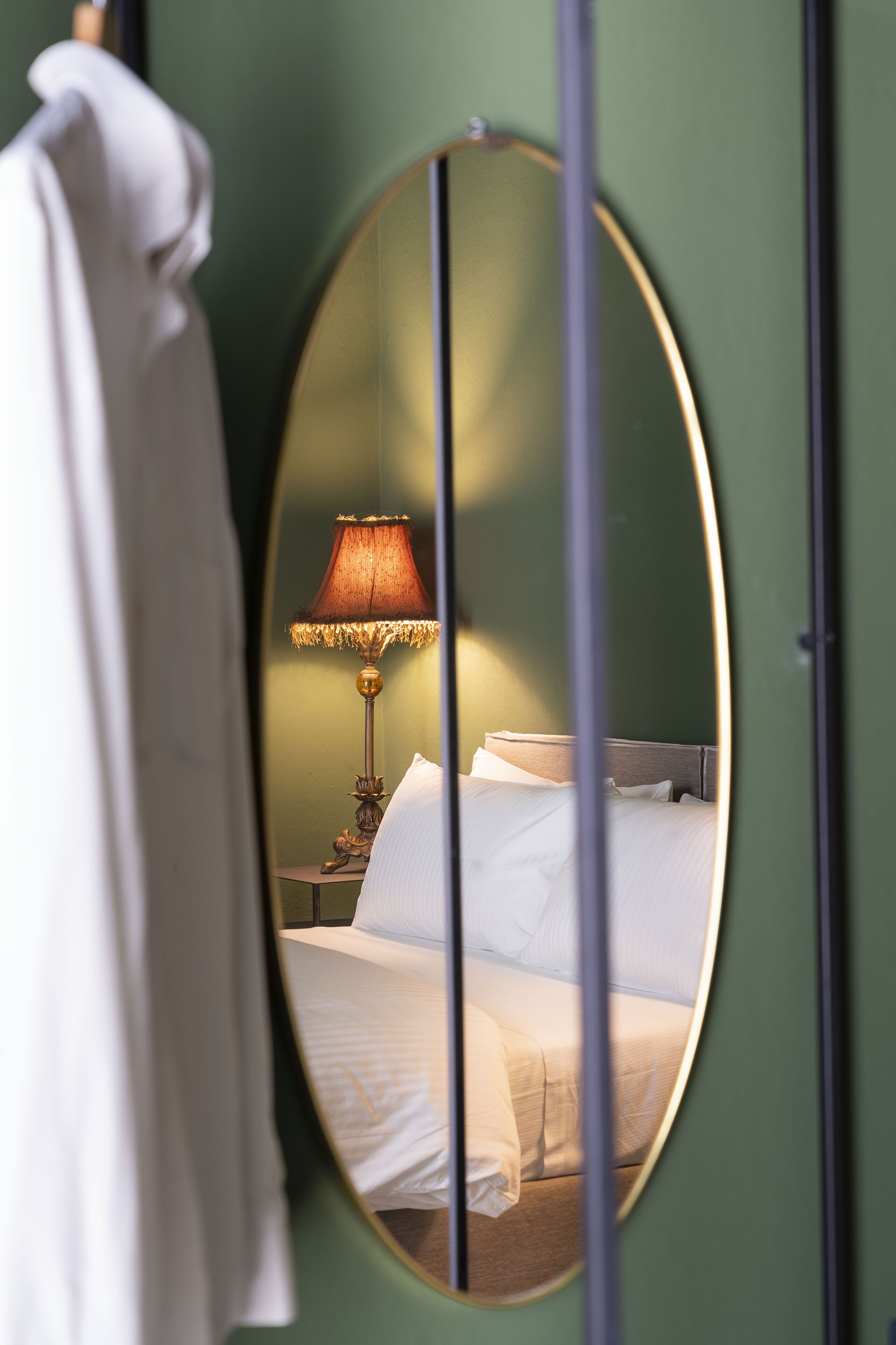 A room with a bed, a lamp, and a mirror reflecting the bed and lamp.