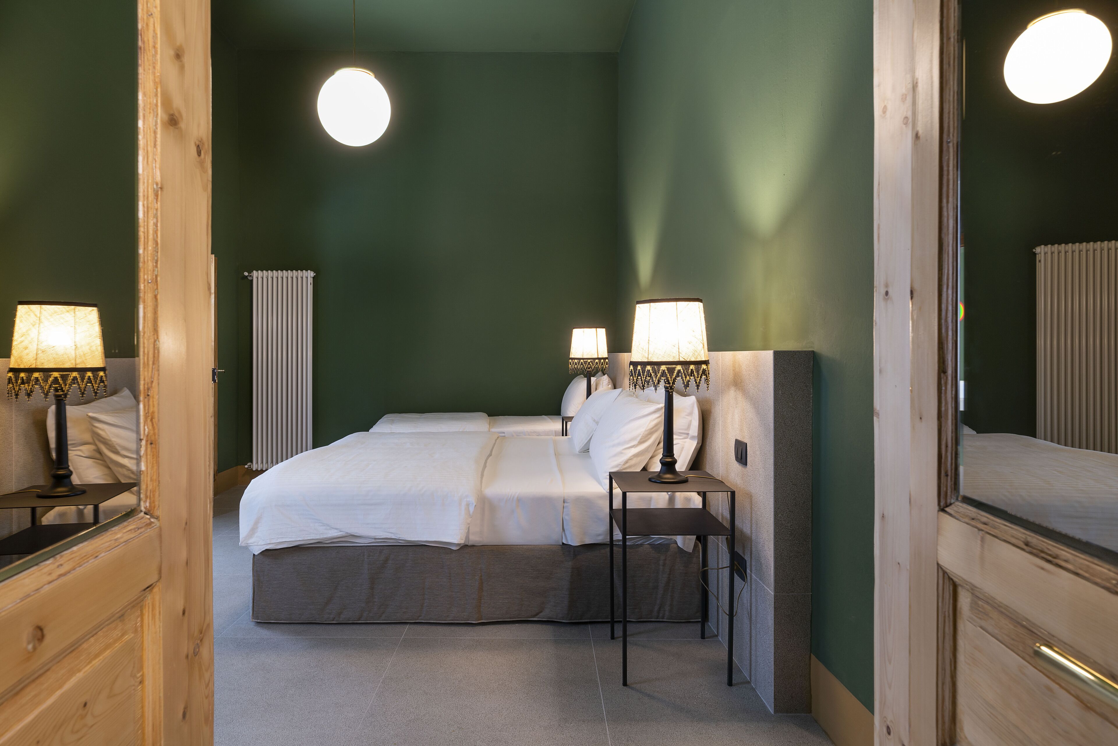 Ein Hotelzimmer mit einem Bett, zwei Nachttischlampen, einem Holznachttisch, einem Heizkörper und einem Spiegel.