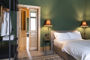 Een hotelkamer met een bed, twee bedlampen, een houten garderobe en een deur naar een andere kamer.