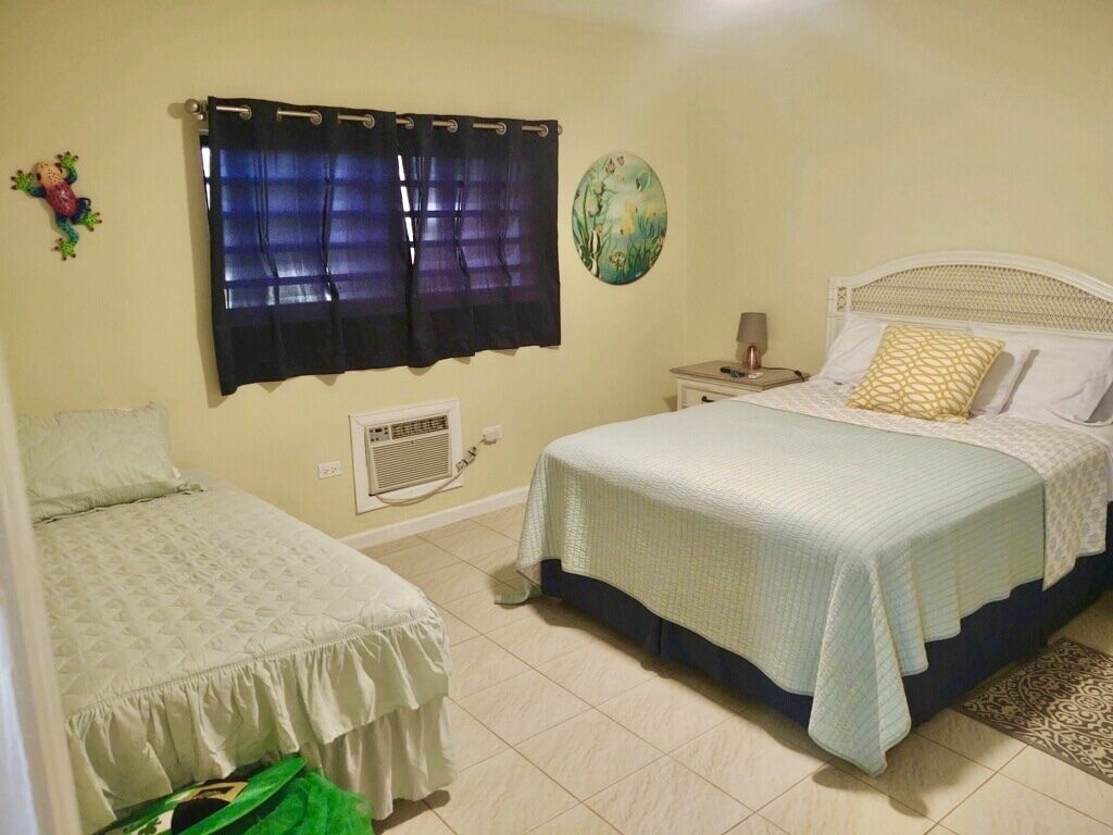 Een slaapkamer met twee bedden, een nachtkastje, een ingebouwde airconditioner en een decoratief bord.