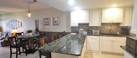 A modern kitchen with white cabinets, a granite countertop, and a dining area with a table and chairs.