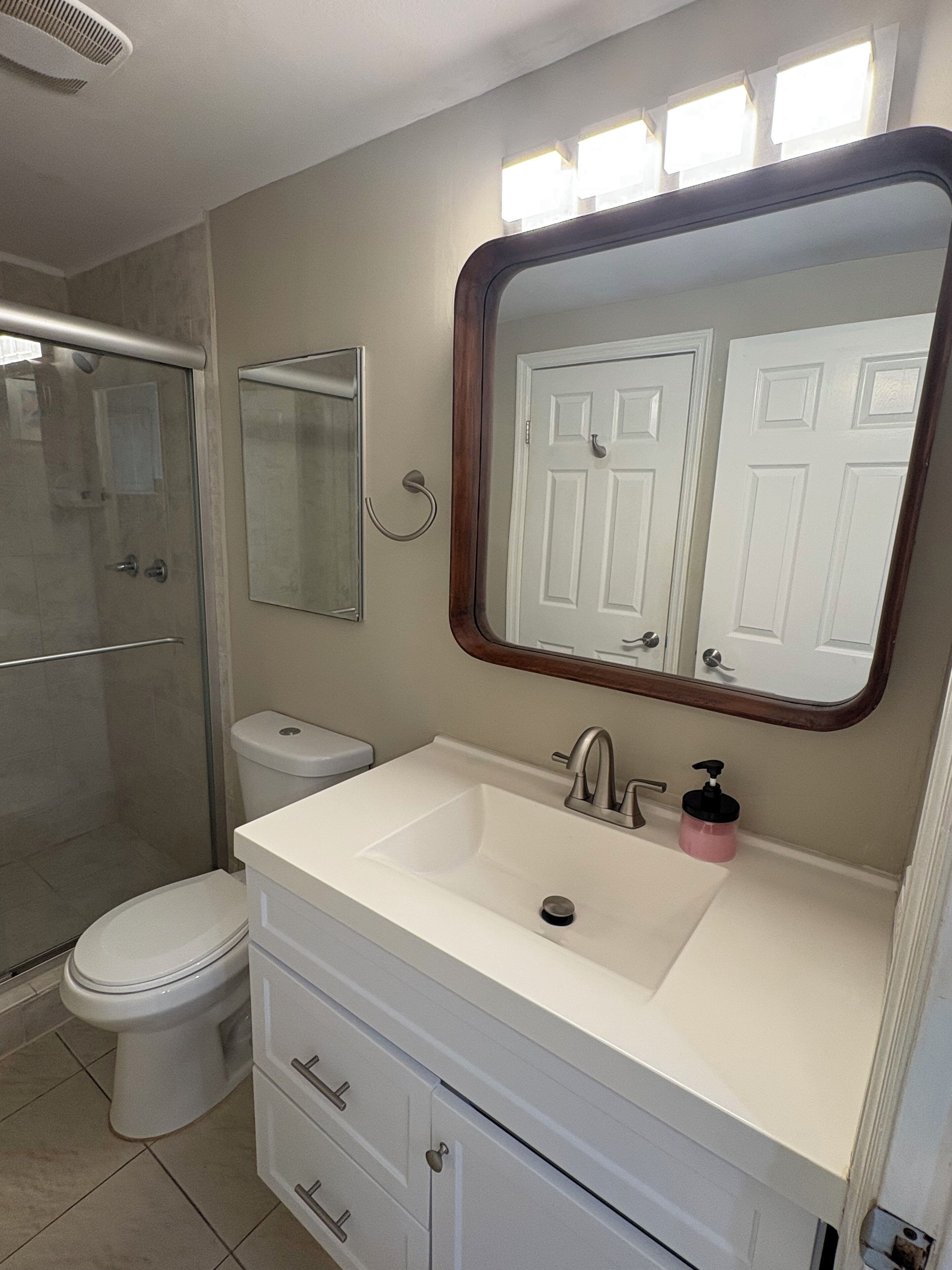 Een badkamer met toilet, wastafel, spiegel en douche.