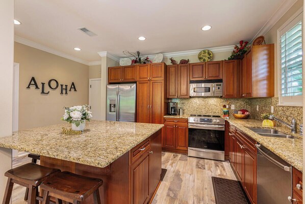 A kitchen with wooden cabinets, granite countertops, stainless steel appliances, and a 'Welcome' sign.