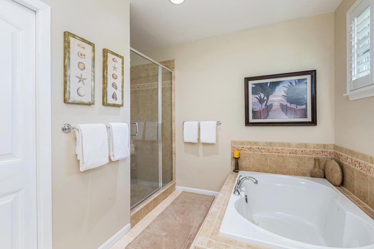 Un baño con una bañera grande, una cabina de ducha de vidrio y dos cuadros en la pared.