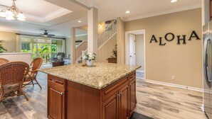 Une cuisine spacieuse avec un grand îlot central, des armoires en bois et un panneau décoratif portant l'inscription « ALOHA » au mur.