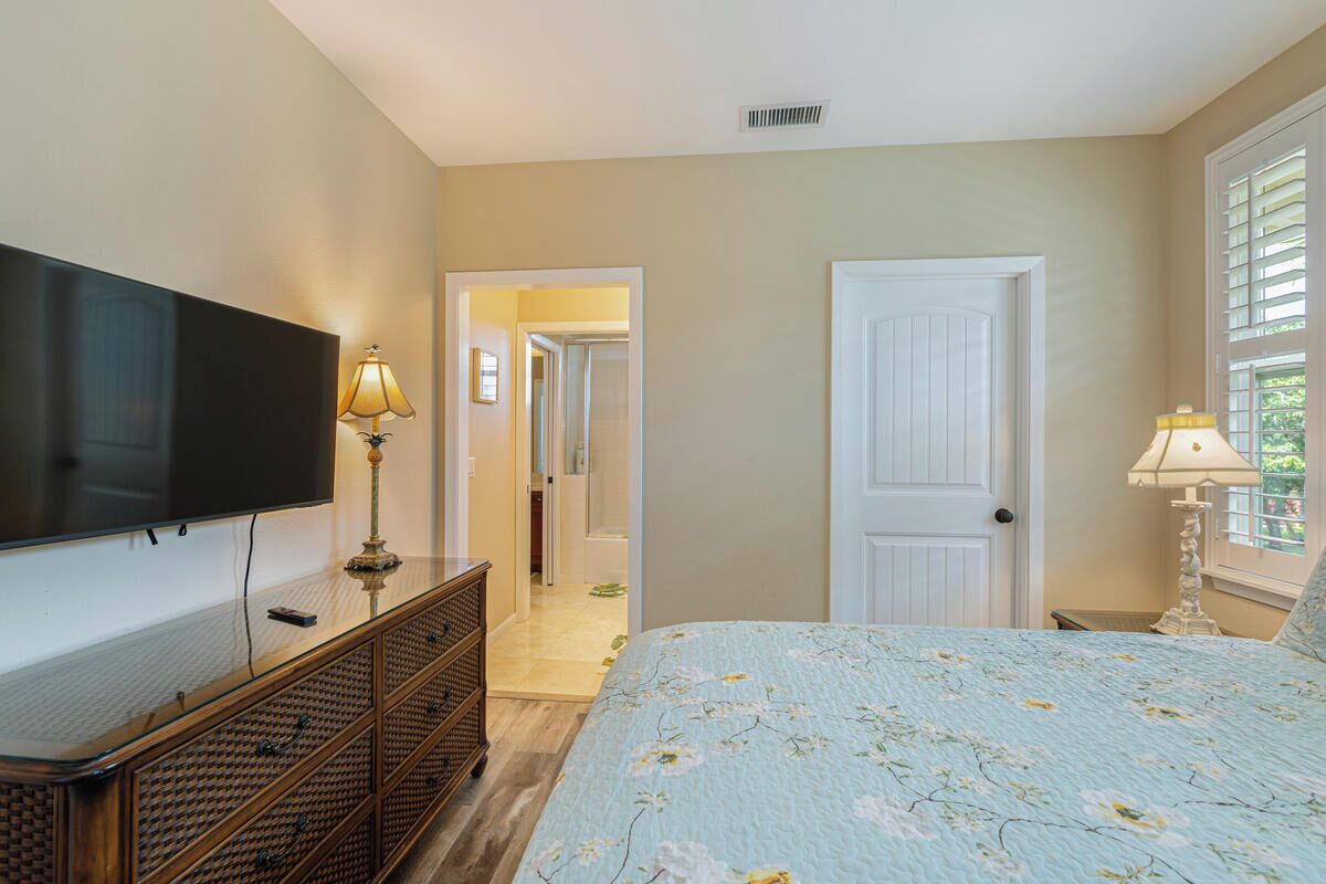 Un dormitorio con una cama, televisión sobre un mueble, una lámpara y una puerta que da a otra habitación.
