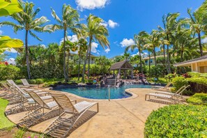 A pool area with lounge chairs, palm trees, and a gazebo.
