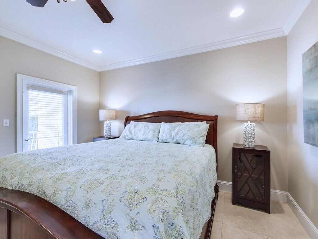 A bedroom with a bed, two bedside lamps, a nightstand, a door, and a window.