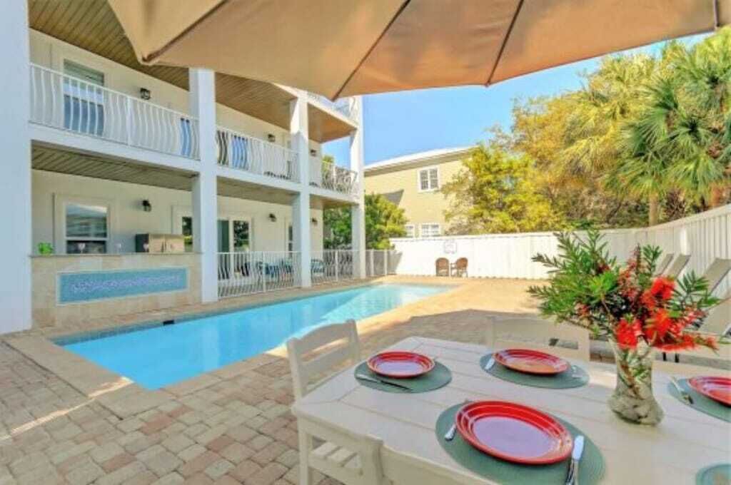 A poolside dining area with a table set for four, surrounded by a white building with balconies.