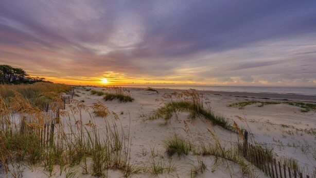 Una playa con dunas de arena y un atardecer.