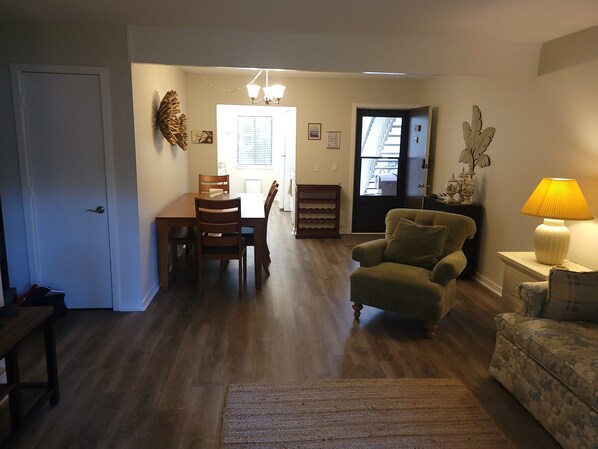 A living room with a sofa, a chair, a dining table with chairs, a lamp, and a door leading to another room. - Comfy Island House Villa - Just a Walk to the Beach & Coligny (Hilton Head Island)