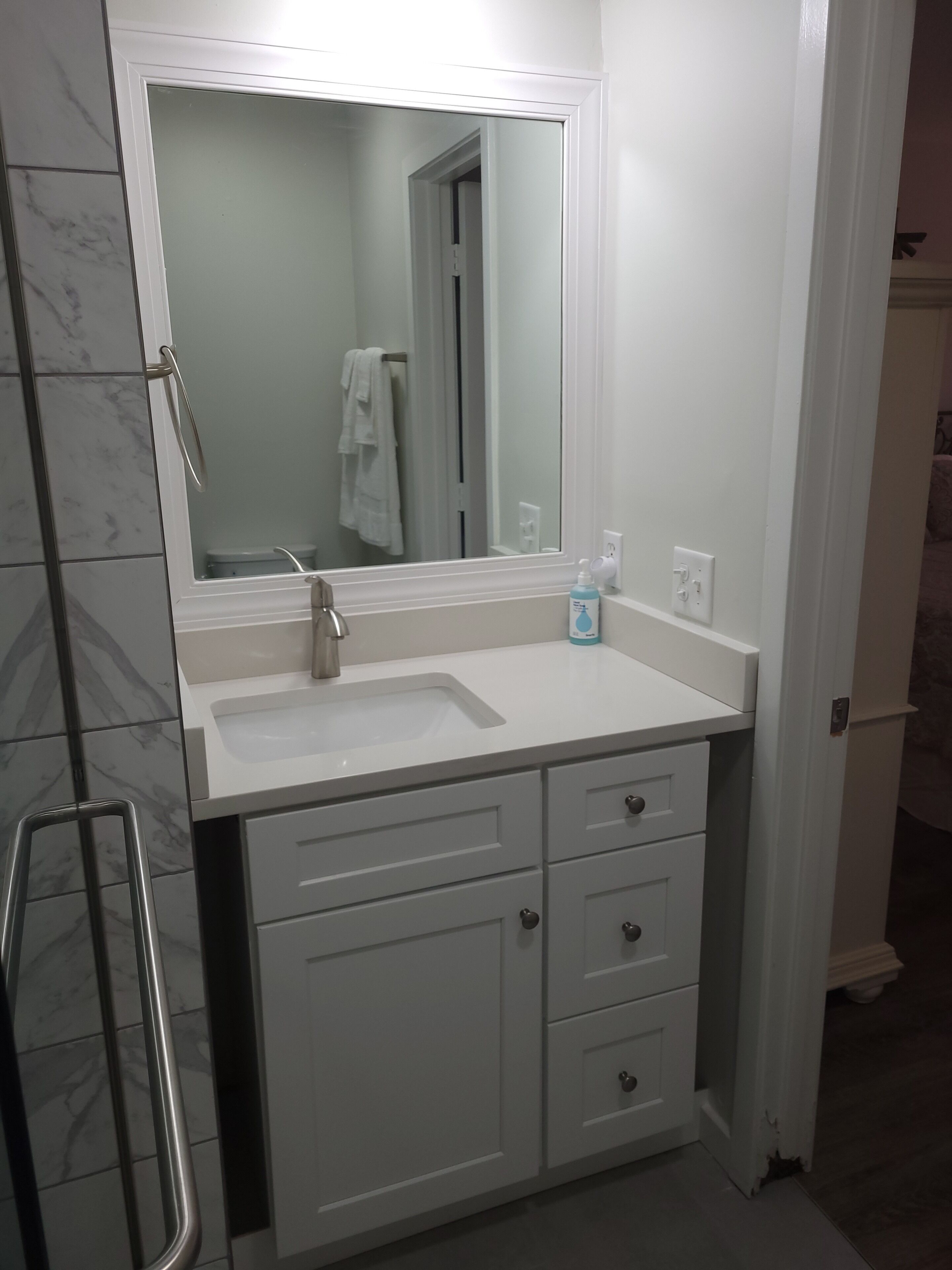 A bathroom with a white sink, mirror, and cabinets.
